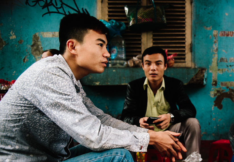Two young Vietnamese men sit together outside in Hanoi