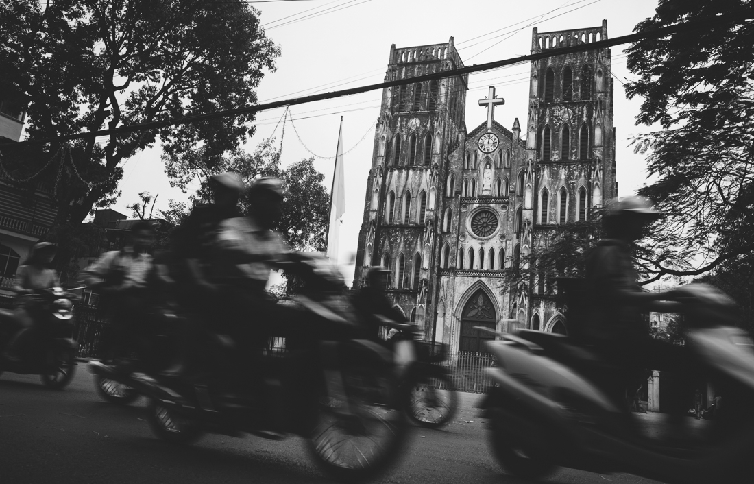 Motorcycles zoom past a cathedral in Hanoi's old town