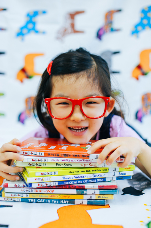 Smiling young girl smiles while holding a stack of Dr. Suess books