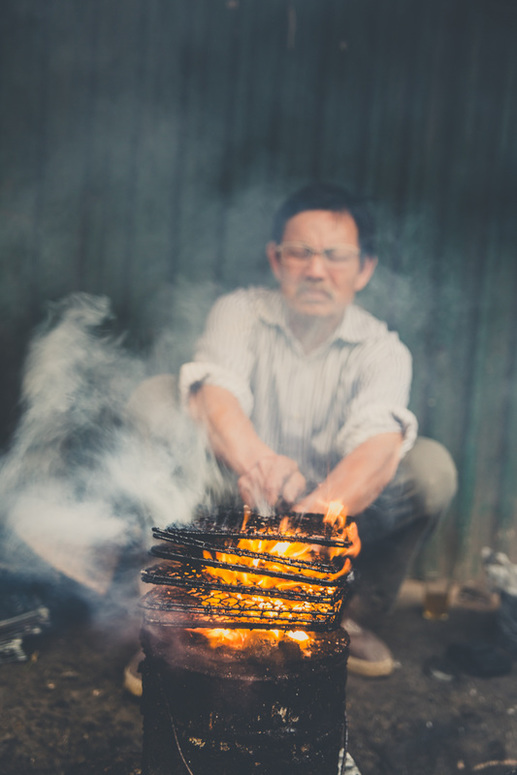 man gets the grease off of his grills by holding them over a fire on the street in Hanoi