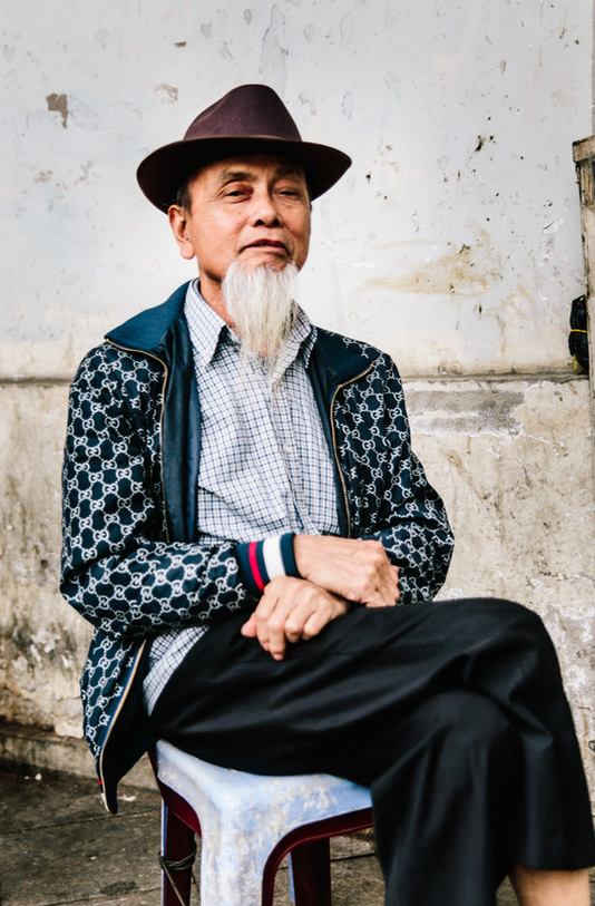 Old Vietnamese man with a beard sits on a plastic seat on the street in Hanoi