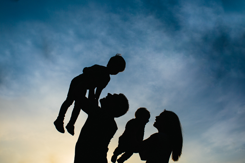 silhouette of parents holding kids up  in the sky
