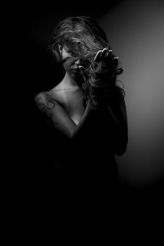 Monochrome nude portrait of woman stretching her hair with heavy shadows