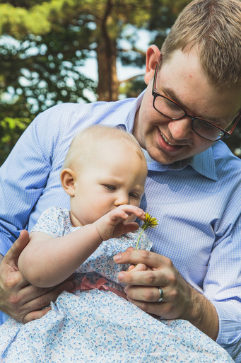father holds daughter while she plaus with a dandelion