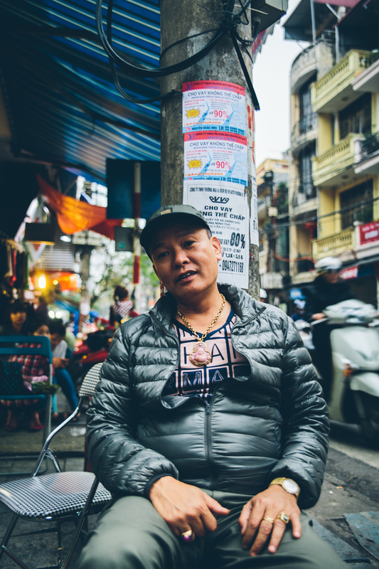 Vietnamese man with large necklace sits on the street