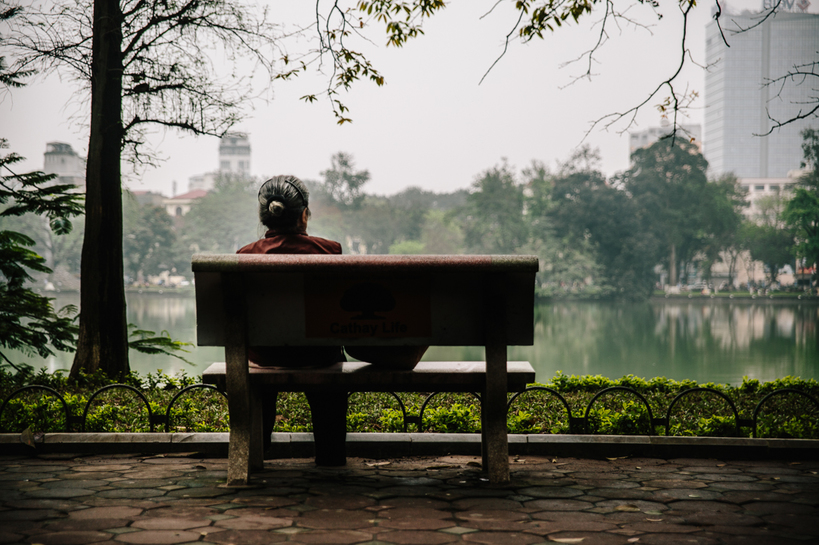 Lone woman sits by herself on a bench next to Hoan Kiem lake 
