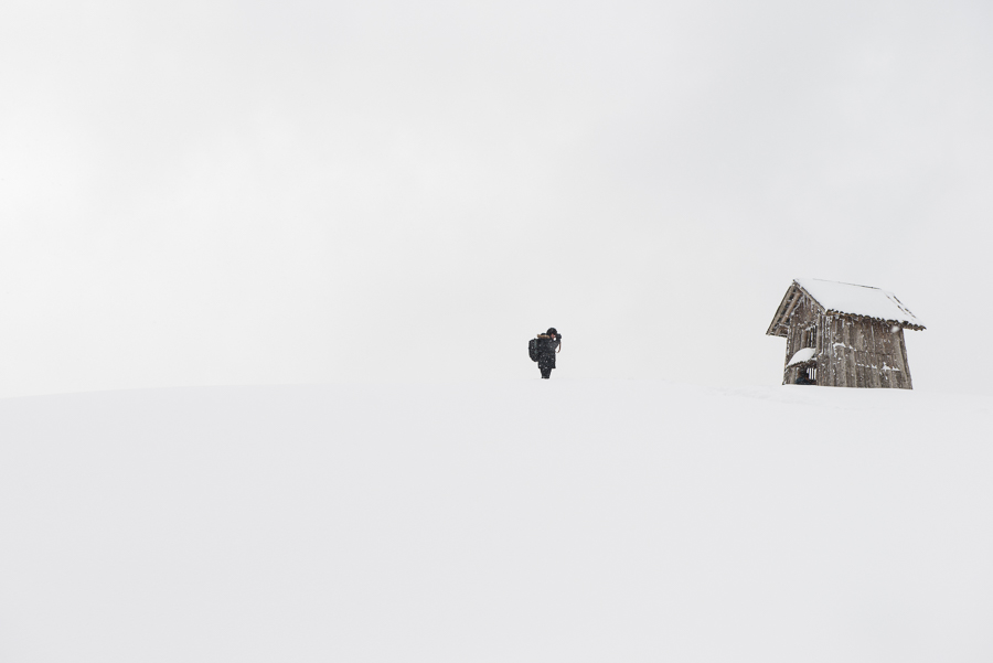 lone man in snow next to wooden shed