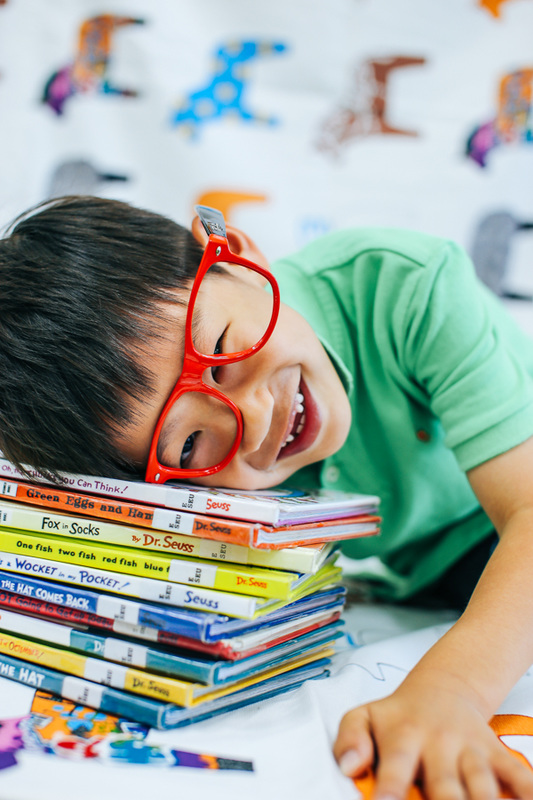 Kid with glasses lays on a pile of Dr. Suess books