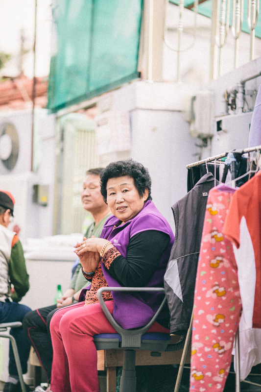 Korean woman smiles for her portrait to be taken outside of her street side store